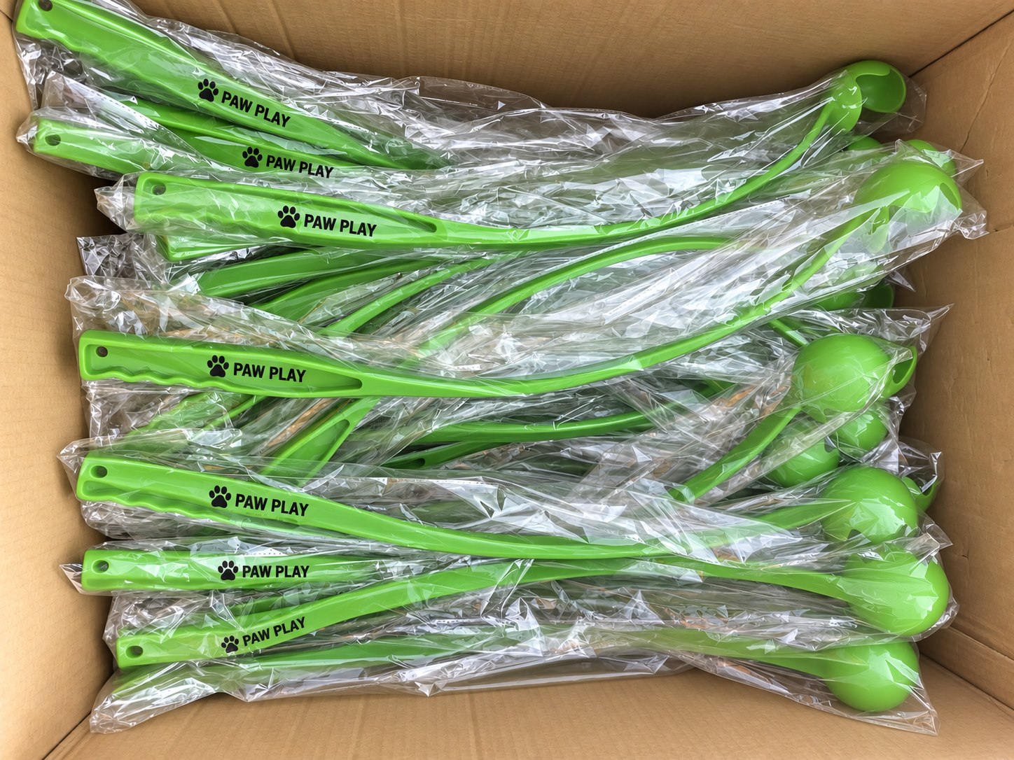 Individually bagged green dog ball launchers packed in a carton with anonymized logos