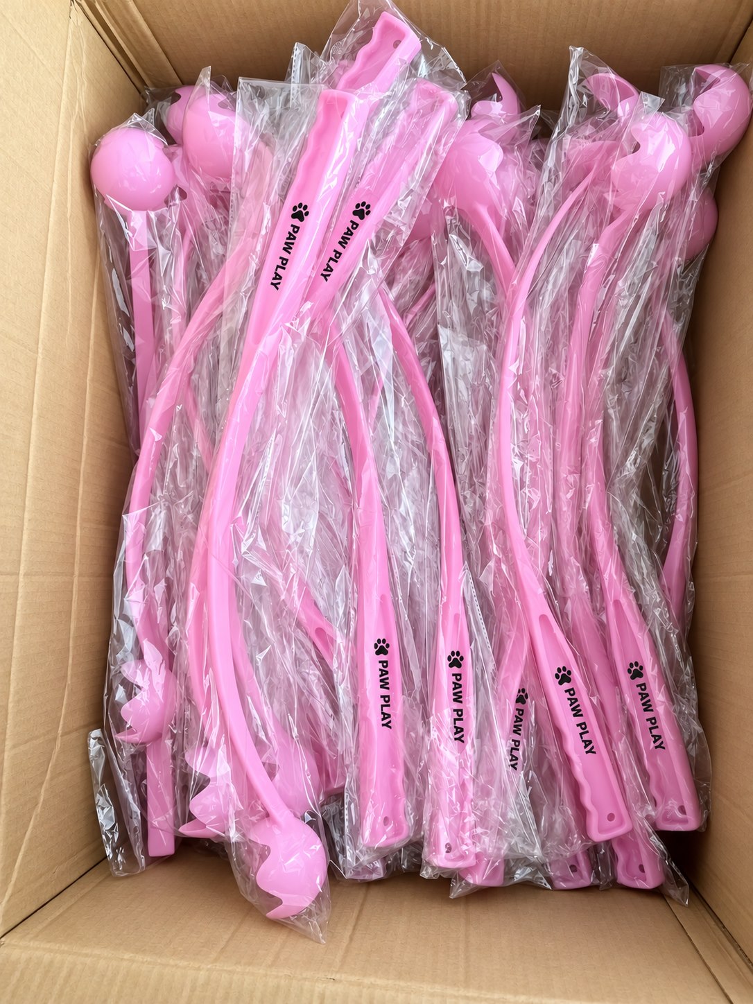 Individually bagged pink dog ball launchers packed in a carton with anonymized logos